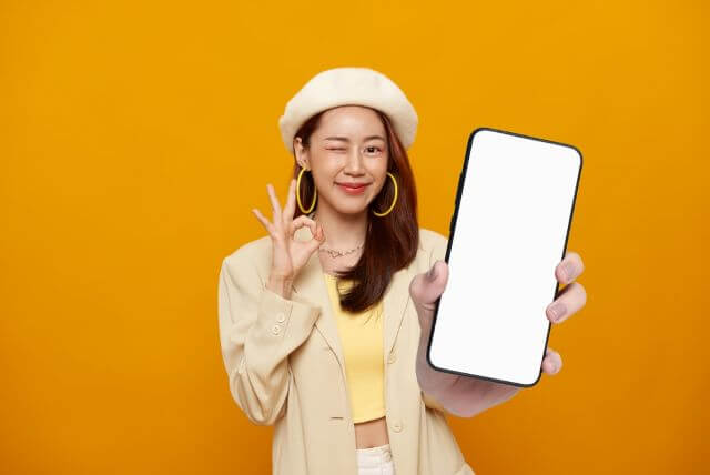 携帯の画面をこちらに向けてOKサインをする女性